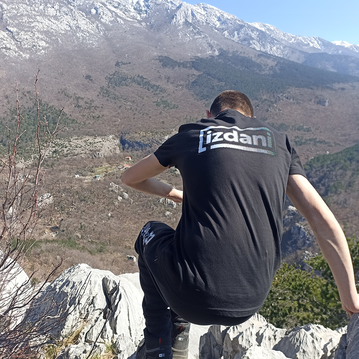 A participant in an IZDANI T-shirt sits on rocks, looking towards the mountains