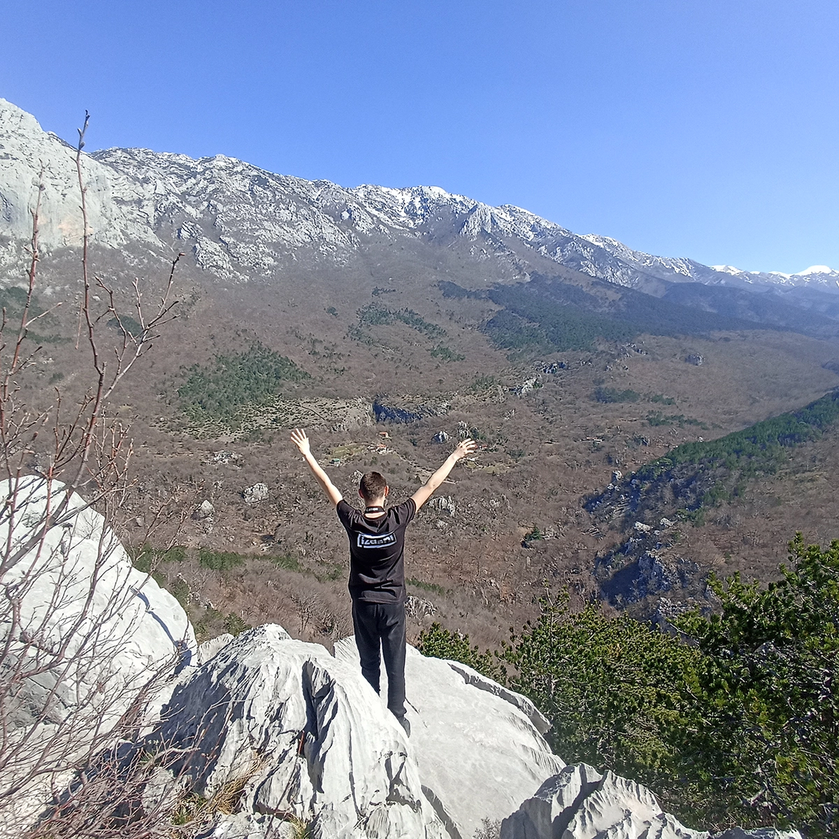 A participant with arms raised on the rocks, overlooking the mountains