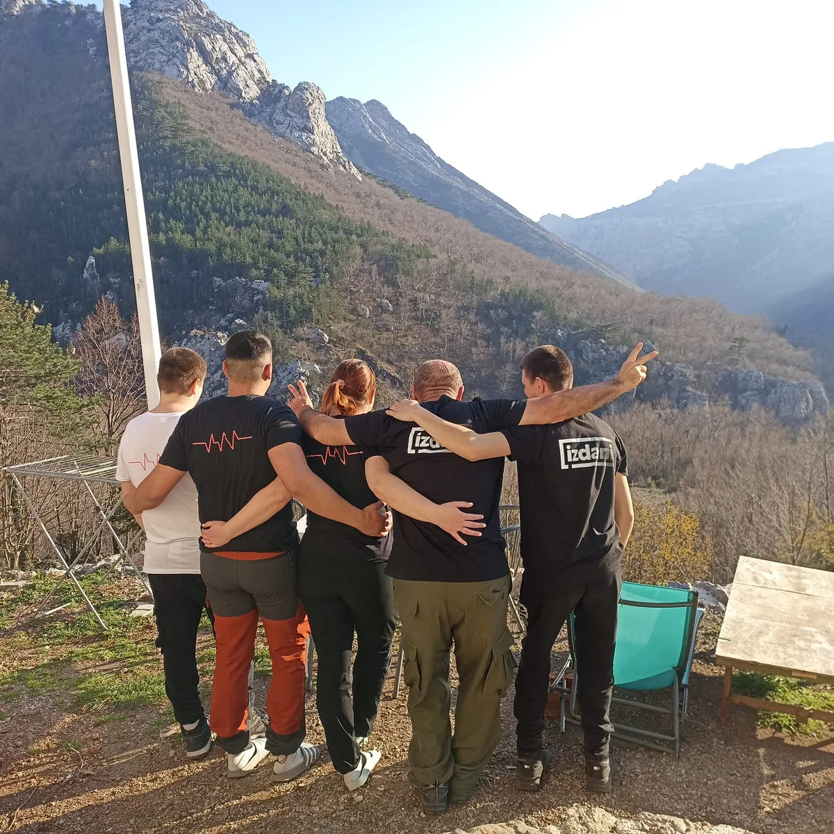 A group of participants arm in arm, seen from behind, looking towards the mountains