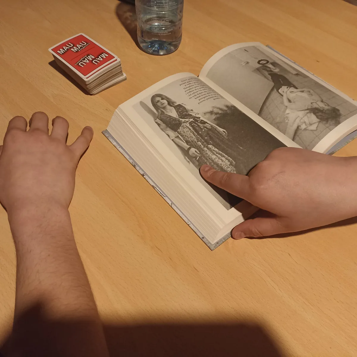An open book and MAU MAU playing cards on a wooden table