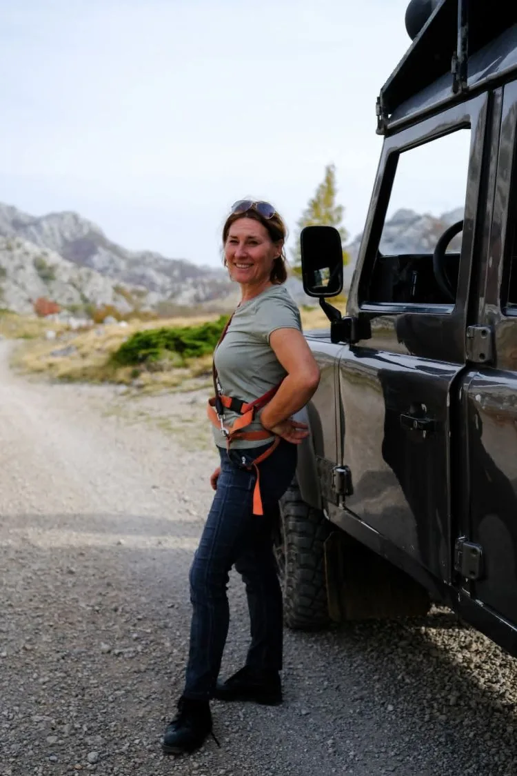 A smiling woman beside an off-road vehicle on a mountain road