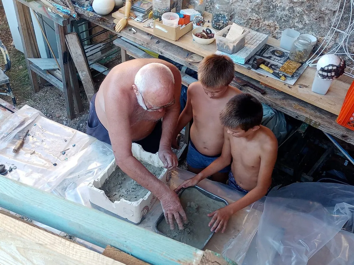 An older man and two boys working with clay in a workshop